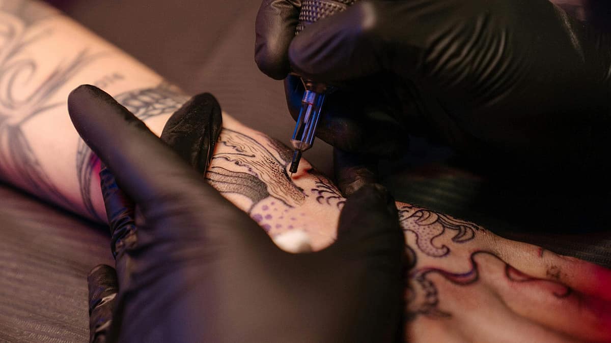 Tattoo artist sketching a cover-up design over an old tattoo