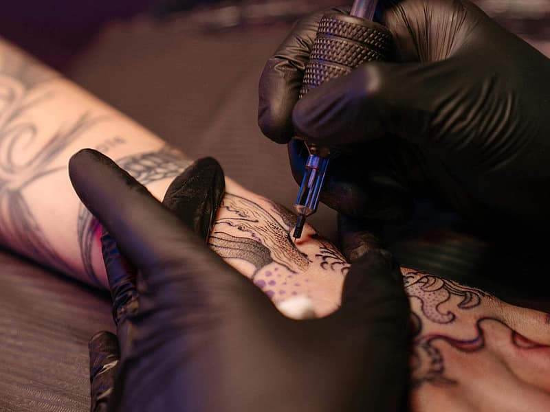 Tattoo artist sketching a cover-up design over an old tattoo