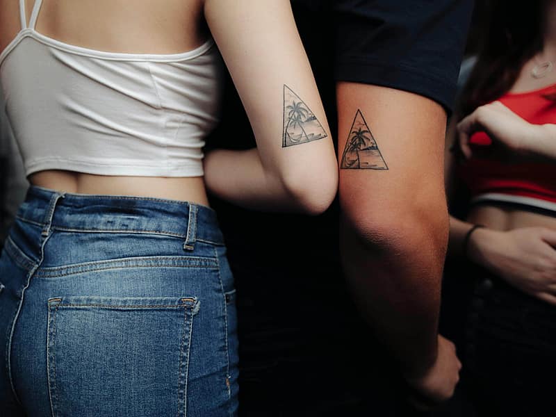 Two friends comparing small matching tattoos on their arms