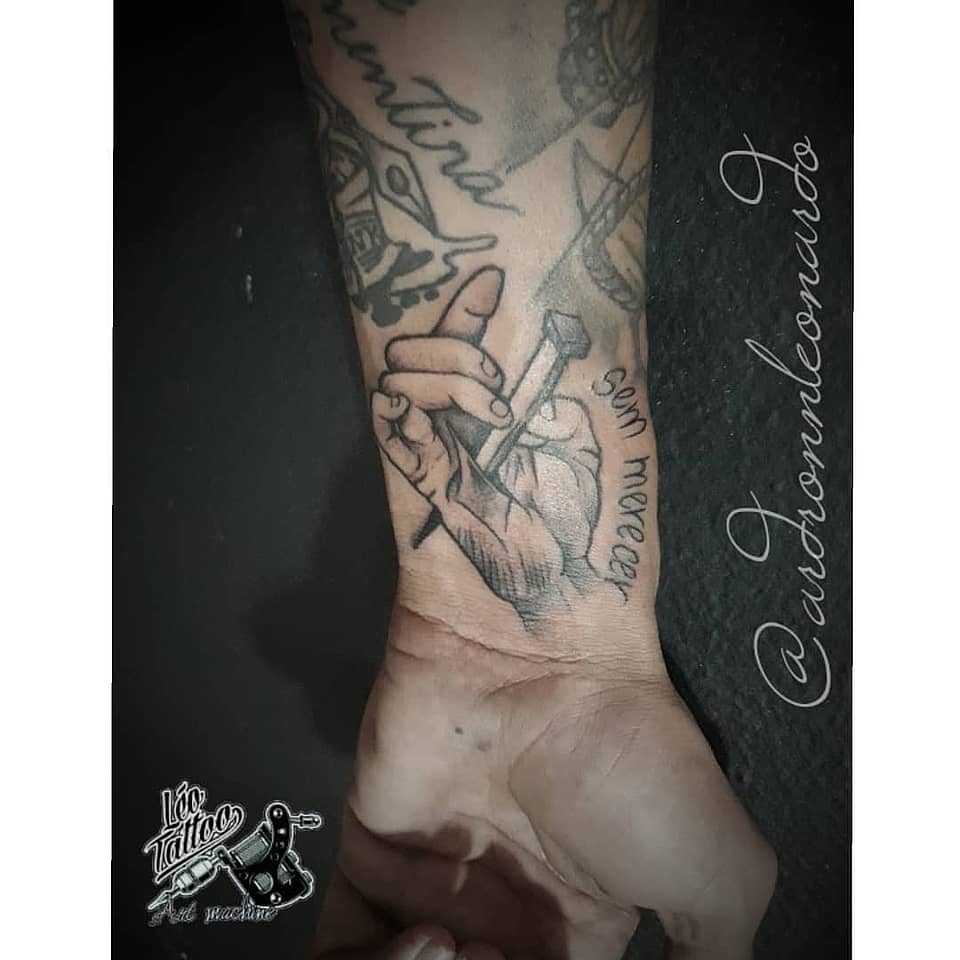 Hand Holding Nail — Fine Line Wrist Tattoo